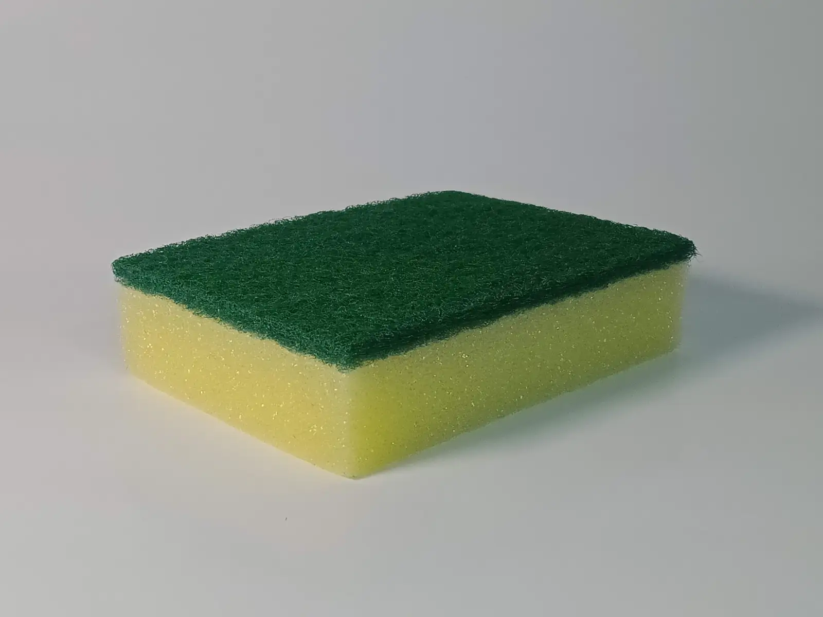 A yellow sponge with a green scouring pad on a white surface